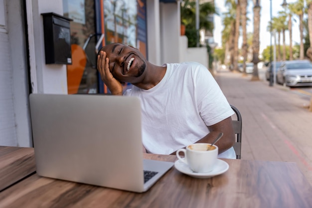 Alegre homem étnico com laptop no café