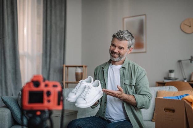 Alegre homem europeu idoso blogueiro com barba registra revisão de vídeo em sapatos descompacta compras