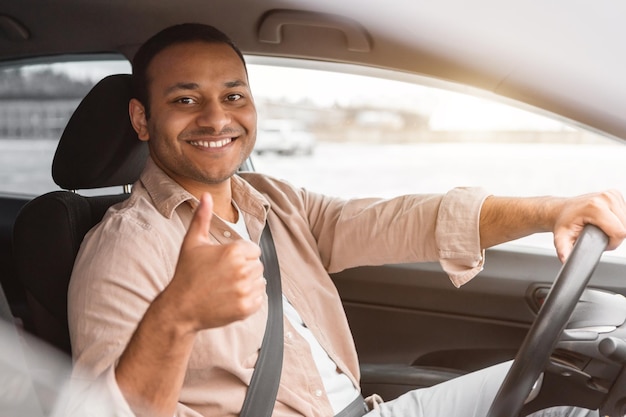 Alegre homem indiano desfrutando de viagens de carro gesticulando polegares para cima