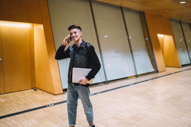 Alegre homem moderno falando no telefone e segurando o laptop