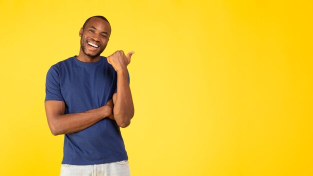 Foto alegre homem negro apontando o polegar para cópia espaço fundo amarelo