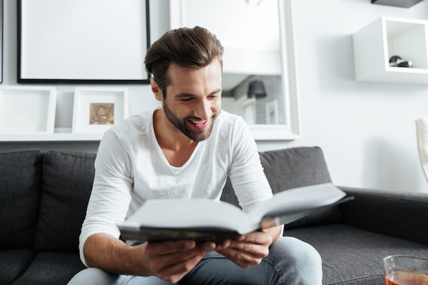 Alegre homem sentado no sofá lendo livro