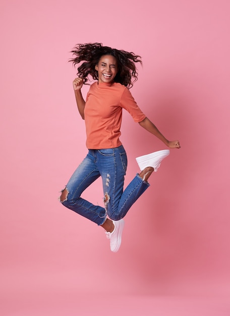 Foto alegre jovem africana na camisa laranja, pulando e comemorando o rosa.