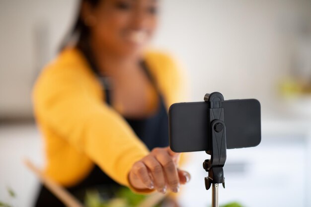 Foto alegre jovem afro-americana blogueira em avental preparando salada à mesa com legumes gravar vídeo