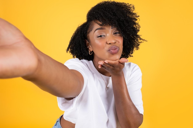 Alegre jovem afro-americana encaracolada fazendo beijo e selfie se divertindo