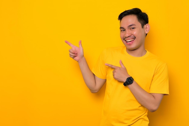 Alegre jovem asiático em camiseta casual apontando o dedo de lado no espaço de cópia isolado em fundo amarelo Grande conceito de oferta