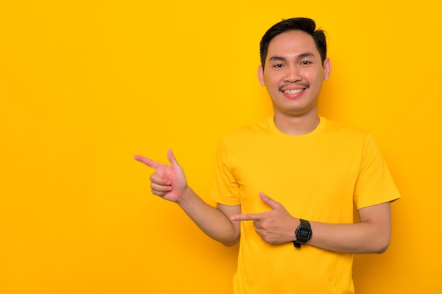 Alegre jovem asiático em camiseta casual apontando o dedo de lado no espaço de cópia isolado em fundo amarelo Grande conceito de oferta