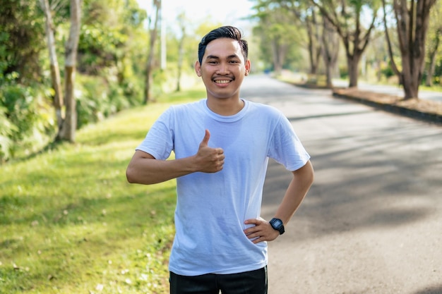 Alegre jovem asiático mostrando os polegares para cima gesto na natureza Estilo de vida saudável