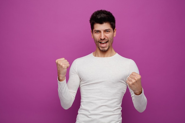 Alegre jovem bonito olhando para a câmera fazendo sim gesto no fundo roxo