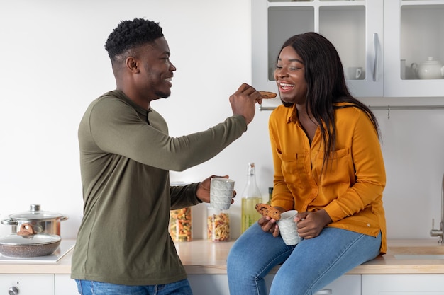 Alegre jovem casal negro comendo lanches na cozinha aconchegante juntos