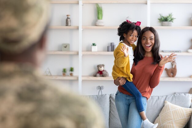 Alegre jovem esposa negra e filha dando as boas-vindas ao pai militar em casa