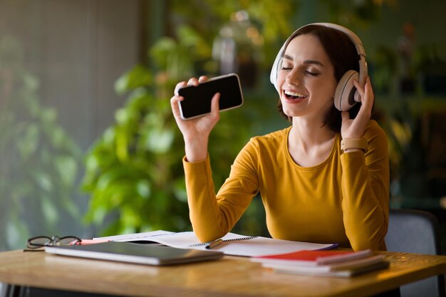 Alegre jovem freelancer trabalhando no café cantando com telefone