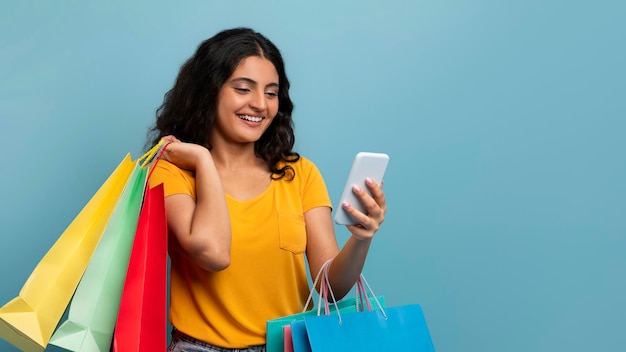 Alegre jovem indiana com telefone e sacolas de compras