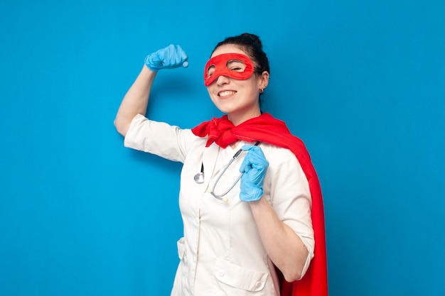 Alegre jovem médica de uniforme em traje de super-homem em super-heroína de enfermeira feminina de fundo azul