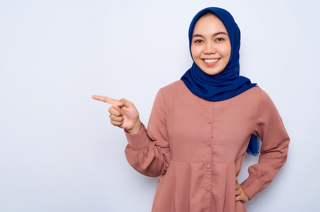 Alegre jovem muçulmana asiática na camisa rosa, apontando os dedos de lado no espaço da cópia isolado sobre o fundo branco Pessoas conceito de estilo de vida religioso