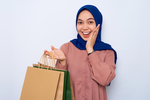 Alegre jovem muçulmana asiática na camisa rosa segurando sacos de pacote com compras após as compras isoladas sobre fundo branco Conceito de estilo de vida de pessoas