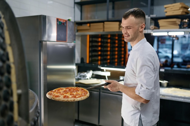 Alegre jovem trabalhando na pizzaria apresentando pastelaria fresca. Chef cozinhando fast-food italiano no restaurante