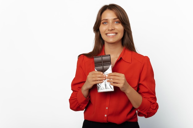 Alegre jovem vestindo camisa vermelha segurando uma barra de chocolate aberta