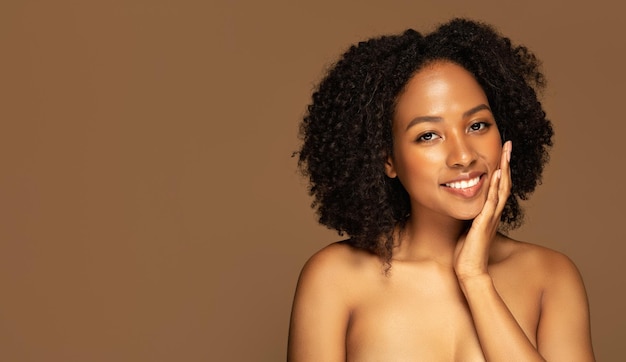 Alegre joven afroamericana semidesnuda tocándose la cara