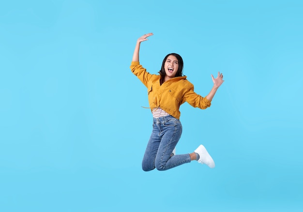 Foto alegre joven asiática en camisa amarilla saltando y celebrando sobre azul.