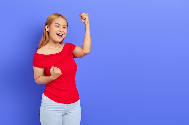 Alegre joven asiática celebrando la victoria, eufórica por los logros en el fondo morado