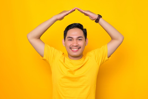 Alegre joven asiático en camiseta casual haciendo azotea con las manos sobre la cabeza aislado sobre fondo amarillo Concepto de estilo de vida de la gente