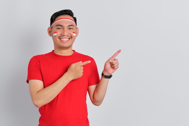 Alegre joven asiático celebrando el día de la independencia de Indonesia señalando a un lado el espacio de copia aislado en el fondo blanco