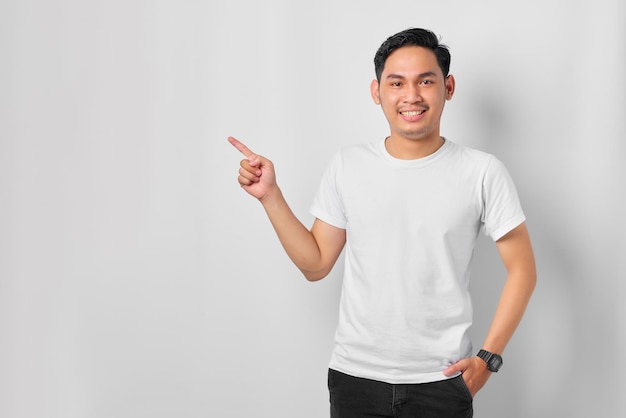 Alegre joven asiático señalando con el dedo el banner publicitario del espacio de copia aislado en el fondo blanco