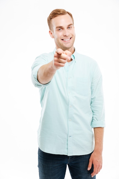 Alegre joven atractivo sonriendo y apuntando al frente sobre la pared blanca