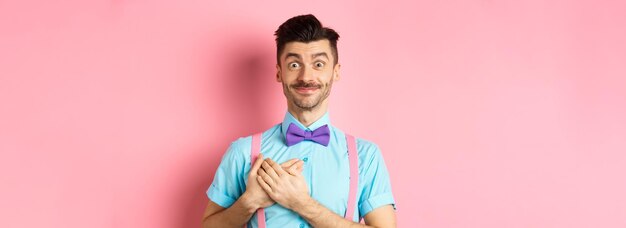 Alegre joven con bigote con camisa y pajarita cogidos de la mano en el corazón y sonriendo gratef