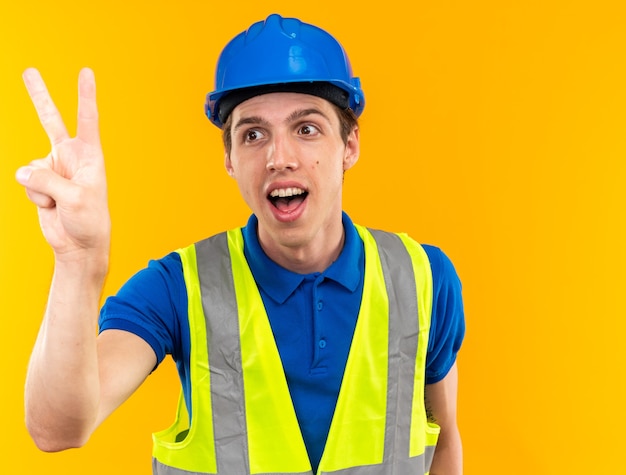 Alegre joven constructor de uniforme mostrando dos