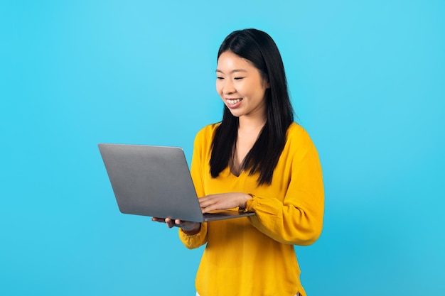 Alegre joven coreana usando una computadora portátil sobre fondo azul
