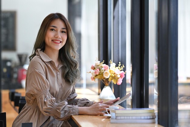 Alegre joven empresaria asiática sosteniendo tableta digital y sonriendo a la cámara