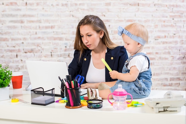 Alegre joven empresaria hermosa mirando portátil mientras está sentado en su lugar de trabajo con ella