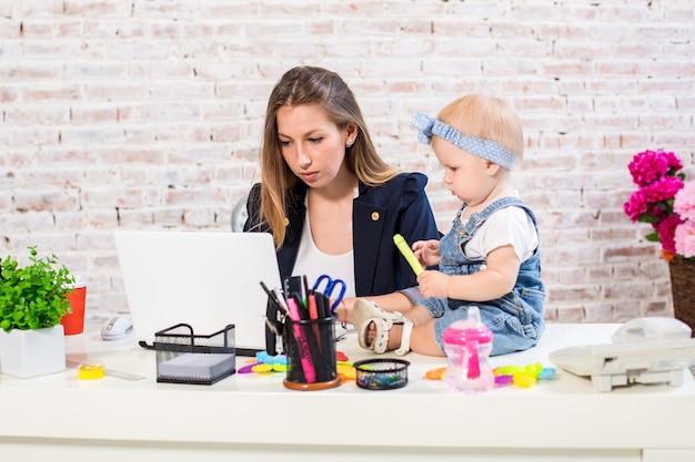 Alegre joven empresaria hermosa mirando portátil mientras está sentado en su lugar de trabajo con ella