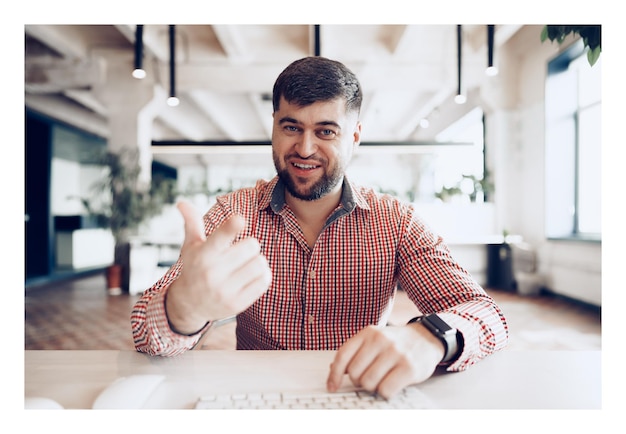 Alegre joven empresario sentados frente al escritorio mirando a la cámara