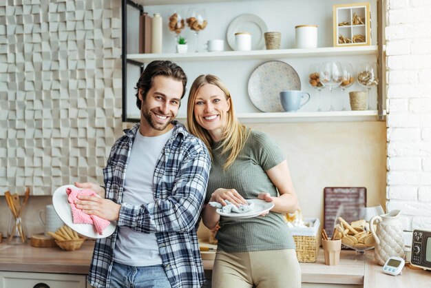 Alegre joven europea y hombres lavando platos en la cocina moderna hogar de higiene interior