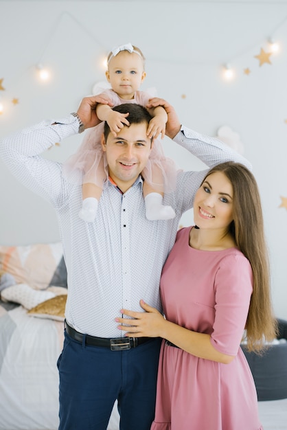 Alegre joven familia feliz con una pequeña hija, que se sienta sobre los hombros de su padre. Padres felices y niñez