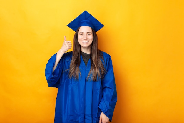 Foto alegre joven feliz graduarse vistiendo de soltero azul y mostrando el pulgar hacia arriba gesto