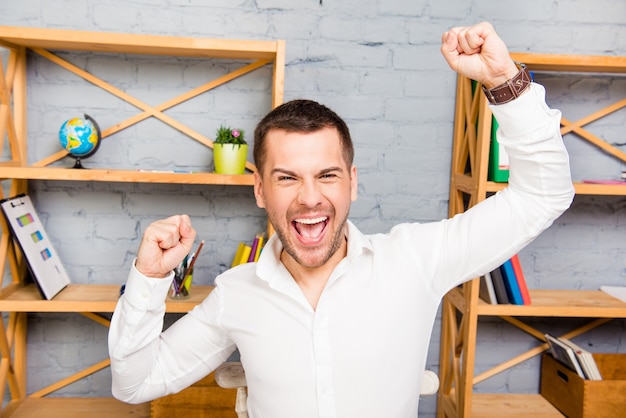 Foto alegre joven feliz triunfando con las manos levantadas