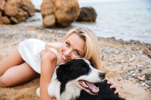 Alegre joven hermosa abrazando a su perro en la playa