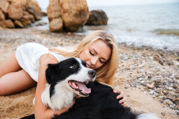 Alegre joven hermosa abrazando a su perro en la playa