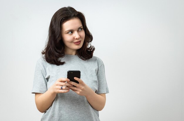 Foto alegre joven hermosa sosteniendo un teléfono celular y mirando lejos espacio de copia