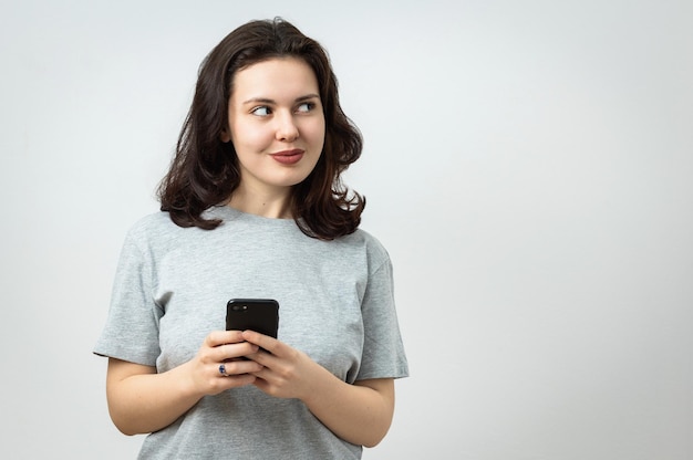 Alegre joven hermosa sosteniendo un teléfono celular y mirando lejos espacio de copia