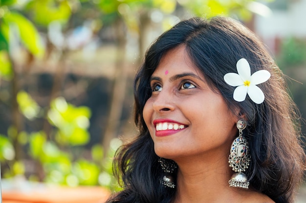 Alegre joven india con flor blanca en el cabello relajándose en la playa en Goa