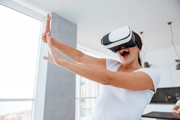 Alegre joven juguetona jugando juegos de computadora con gafas de realidad virtual en casa