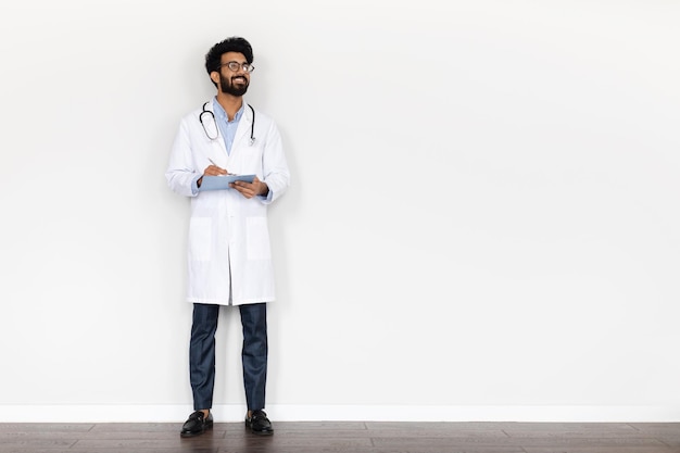 Alegre joven médico indio con carpeta médica fondo blanco.