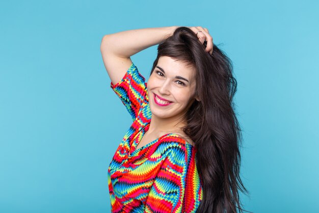 Alegre joven morena con cabello largo posando sobre una pared azul