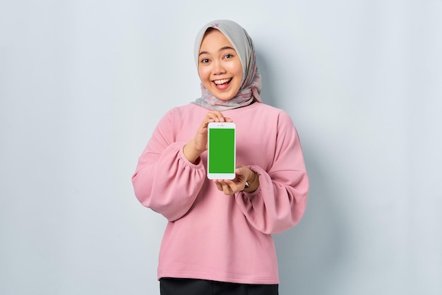 Alegre joven mujer asiática en camisa rosa mostrando la pantalla en blanco del teléfono móvil recomendando la aplicación aislada sobre fondo blanco.