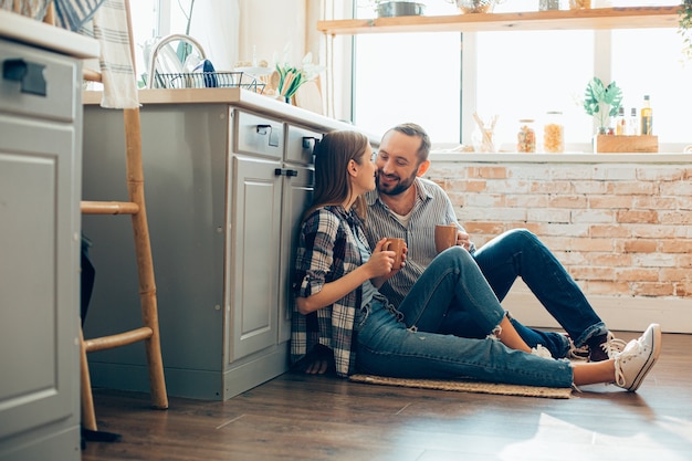 Alegre joven y mujer disfrutando del té de la mañana en la cocina y sonriendo el uno al otro